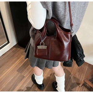 Dettaglio della borsa in pelle lucida bordeaux con manici e ciondolo a catena in metallo