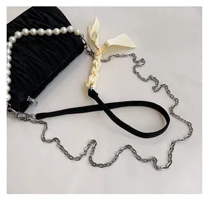 Detail of black pleated velvet bag featuring pearl strap and satin bow chain strap