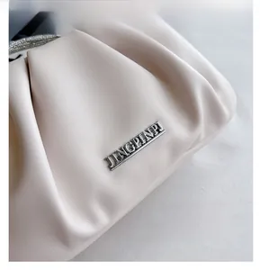 Dettaglio della texture in pelle crema a pieghe con catena di strass e logo argento
