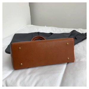 Detail view of the brown leather tote base featuring four golden protective metal feet