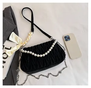 Detail of black pleated shoulder bag with pearl handle and bow showing size comparison