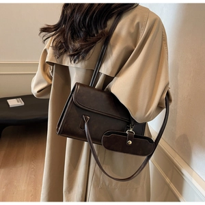 Detail of dark brown vintage shoulder bag with side pouch worn over a beige trench coat