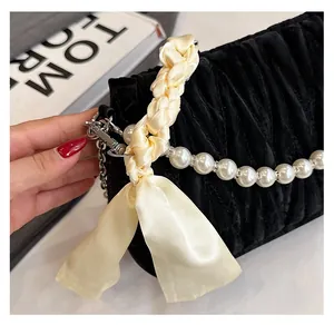 Detail of black quilted handbag featuring a silk scarf handle and pearl chain accessory