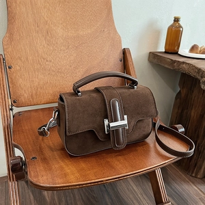 Sac bandoulière en daim marron café sur une chaise en bois vintage, éclairage chaleureux