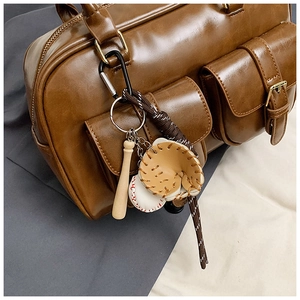 Detailed close-up of a vintage baseball bat and glove keychain charm on a brown leather handbag