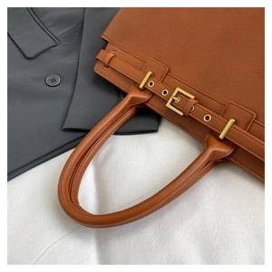 Macro detail of brown leather tote bag showing golden buckle and textured finish