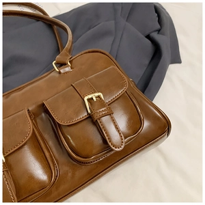 Detailed close-up of glossy brown retro Boston bag with gold buckles and premium stitching