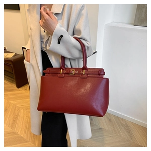 Detail of burgundy leather tote bag with gold buckle hardware in a modern home setting