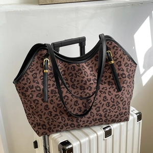 Grande borsa tote leopardata con manici in pelle nera su una valigia bianca da viaggio