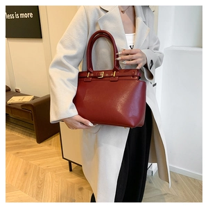 Close-up of burgundy leather tote bag featuring gold buckle details and reinforced handle