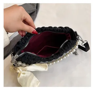 Detail view of black pleated handbag interior with burgundy lining and pearl strap