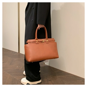 Detail of the brown leather tote bag with gold metal buckle and protective bottom studs