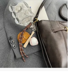 Detail of a baseball glove, bat and ball keychain charm on a brown leather handbag