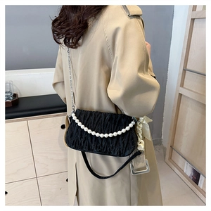Detail of black pleated shoulder bag with pearl handle and ribbon on beige coat