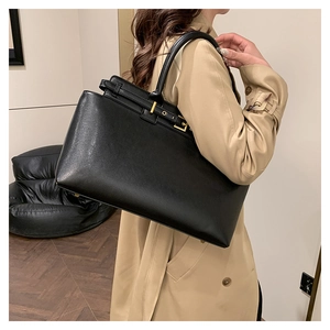 Detail of black leather tote bag with gold hardware worn over the shoulder by a model