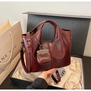 Dettaglio borsa in pelle lucida rosso-marrone con mini ciondolo e tracolla regolabile