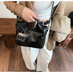 Dettaglio di borsa a mano vintage in pelle nera lucida con cuciture e mini ciondolo lucchetto
