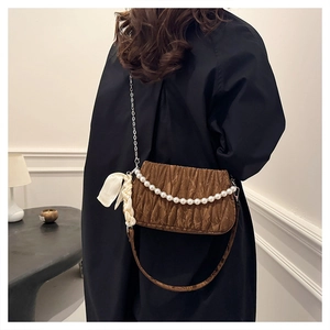 Close-up of brown pleated bag with pearl chain and bow accessory on black coat