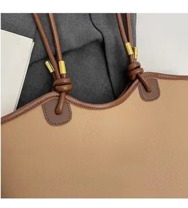 Close-up of beige bucket bag with dark brown knot handle and golden metal buckle accents