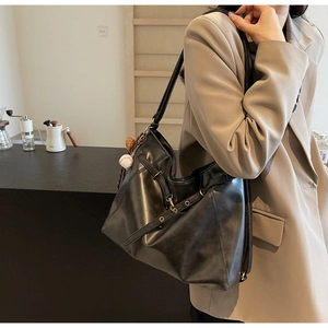 Large black leather tote bag with metal buckles and baseball charm in a cozy cafe