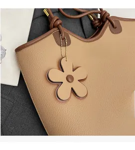 Close-up of light brown lychee grain leather bucket bag with floral charm and logo tag