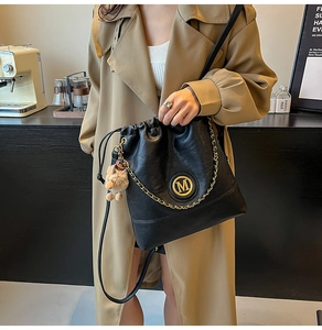 Gros plan du sac seau en cuir noir avec logo M doré, cordon de serrage et pompon