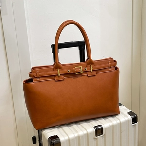 Brown leather oversized tote bag with gold buckle detail on a white suitcase