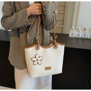 Close-up of cream leather bucket bag with brown trim and floral charm on a model