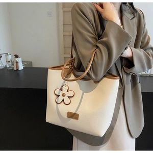 Detail of cream white tote bag with lychee texture, brown leather trim, and floral charm