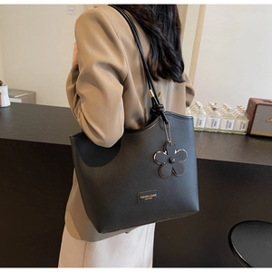 Close-up of black lychee grain bucket bag with gold label and floral charm detail