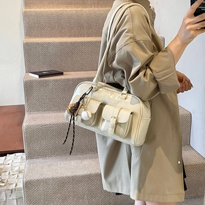 Chic beige glossy Boston bag with front buckle pockets and a trendy baseball charm