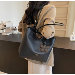 Detail of black lychee grain leather bucket bag with flower charm on indoor counter