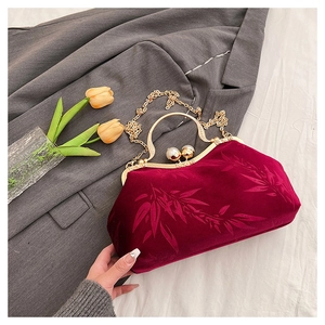 Detail of burgundy velvet clutch with bamboo patterns and pearl clasp on suit jacket