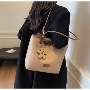 Detail of beige litchi pattern leather bucket bag with elegant flower charm and long strap