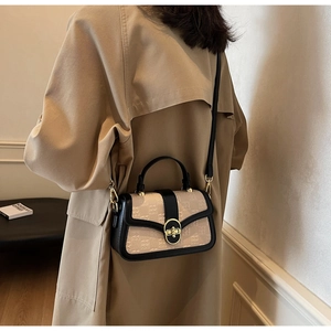 Detail of beige textured messenger bag with black leather trim and golden metal lock