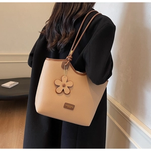 Beige pebble leather bucket bag featuring a side flower charm and adjustable shoulder strap