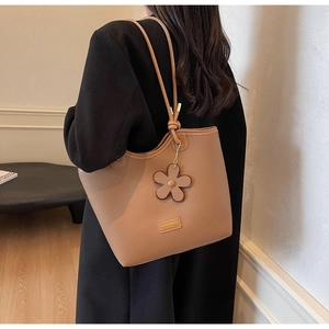 Detail of tan pebble leather bucket bag with floral charm and metallic logo tag
