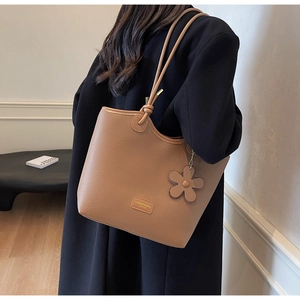 Close-up of brown litchi leather bucket bag with metallic logo and flower charm pendant