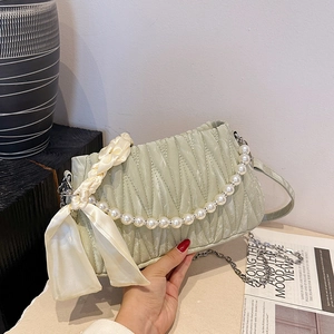 Light green pleated shoulder bag with pearl handle and ribbon detail in a lifestyle setting