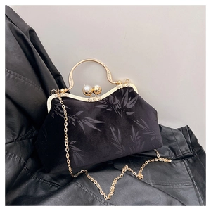 Close-up of velvet handbag with bamboo patterns, gold U-shaped handle, and pearl clasp