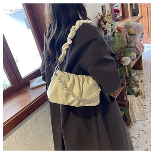 Close-up of cream pleated shoulder bag with large pearl chain and soft leather texture