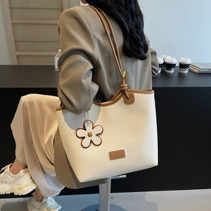 Chic cream bucket bag with brown handles and floral charm in a cafe setting