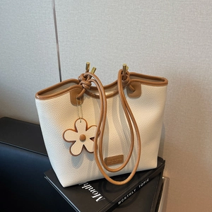 Fashionable off-white bucket bag with brown trim and floral charm on black book