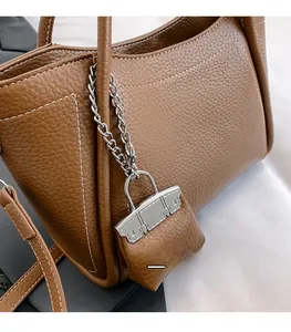 Detail of brown litchi pattern leather handbag with white stitching and silver lock charm