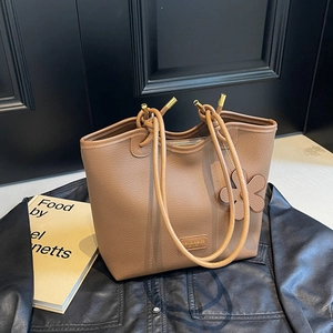 Brown leather bucket bag with knot handle and flower charm on black leather background