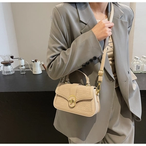 Detail of a beige textured crossbody bag styled with a gray suit in a cozy cafe setting