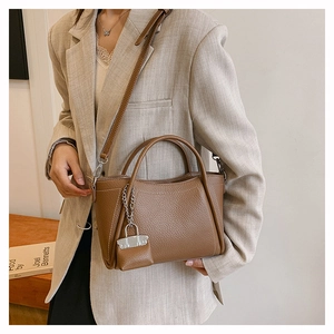 Detail of brown lychee leather handbag with adjustable strap and mini charm pouch