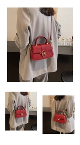 Detail of red embossed leather square bag featuring golden lock and adjustable strap
