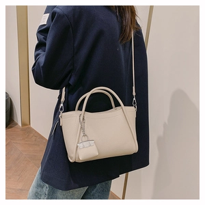 Detail of cream pebbled leather handbag with mini charm and adjustable strap