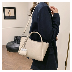 Close-up of beige lychee leather bucket bag with decorative stitching and mini lock charm